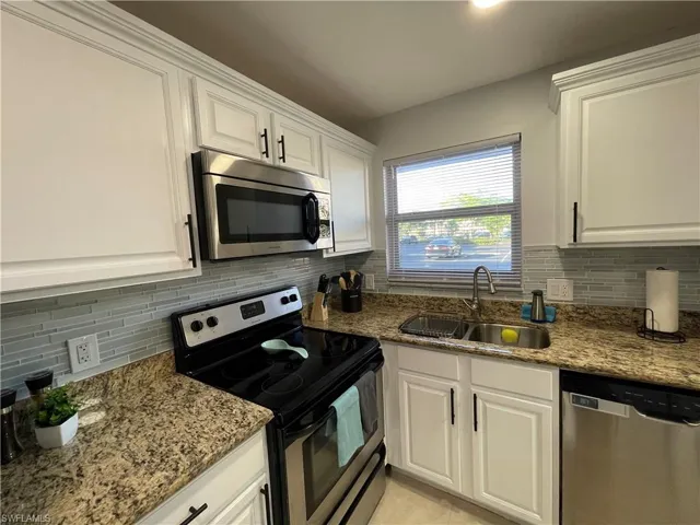 Kitchen featuring appliances with stainless steel finishes, white cabinetry, light stone countertops, and decorative backsplash