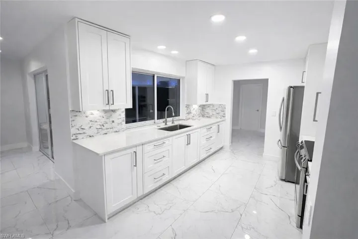 Kitchen with light stone counters, white cabinets, stainless steel appliances, decorative backsplash, and recessed lighting