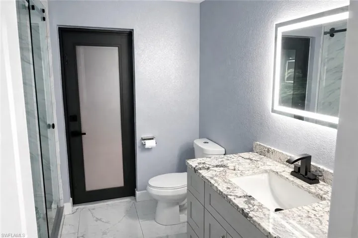 Bathroom featuring vanity, a shower stall, light marble finish flooring, and a textured wall