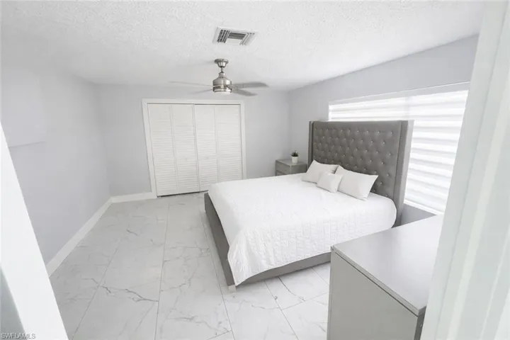 Bedroom featuring light marble finish flooring, a closet, ceiling fan, and a textured ceiling