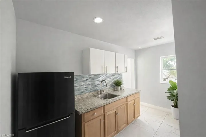 Kitchen featuring freestanding refrigerator, light stone counters, backsplash, light marble finish floors, and recessed lighting