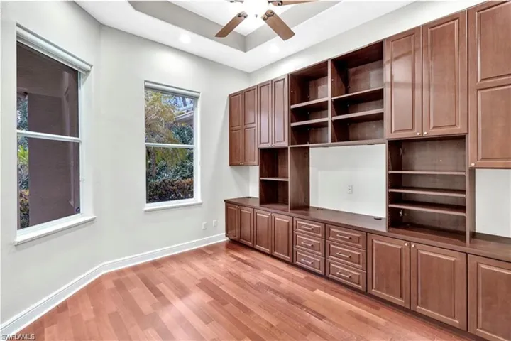 Unfurnished office featuring a tray ceiling, light wood-type flooring, and ceiling fan