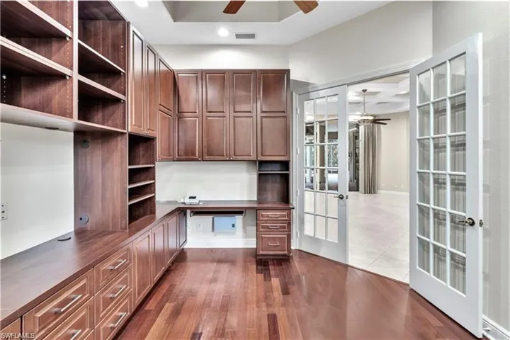 Unfurnished office featuring hardwood / wood-style flooring, built in desk, french doors, and ceiling fan