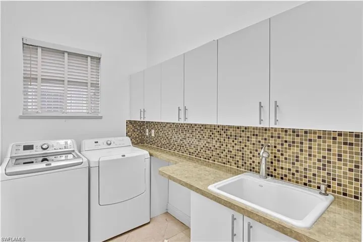 Laundry area featuring light tile patterned floors, washing machine and clothes dryer, cabinets, and sink