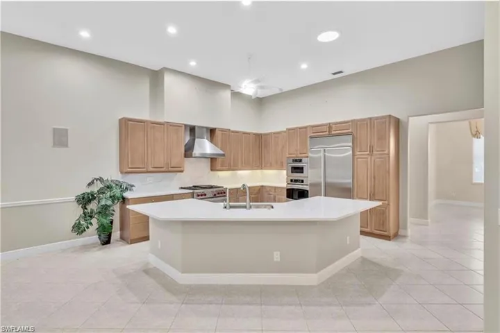Kitchen featuring light tile patterned floors, a kitchen island with sink, stainless steel appliances, wall chimney exhaust hood, and sink