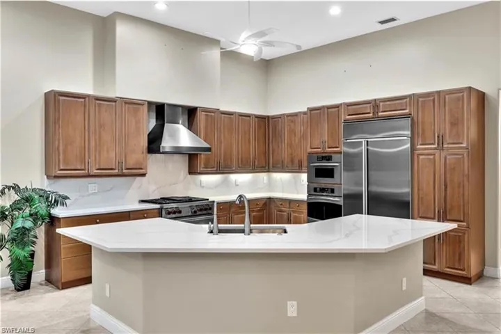 Kitchen with wall chimney exhaust hood, light tile patterned floors, an island with sink, and high end appliances