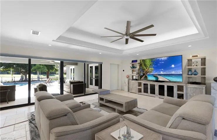 Living room featuring recessed lighting, a ceiling fan, visible vents, a tray ceiling, and stone tile flooring