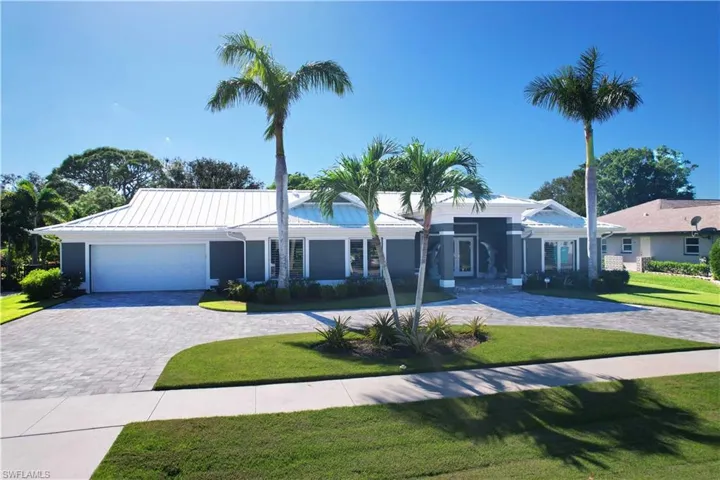 Ranch-style house featuring an attached garage, metal roof, decorative driveway, and a front yard