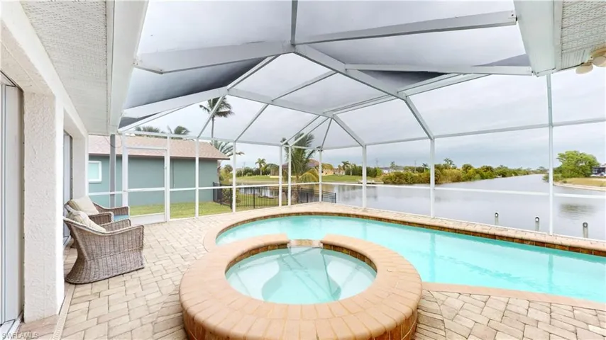 View of swimming pool featuring glass enclosure, a patio area, a water view, and an in ground hot tub