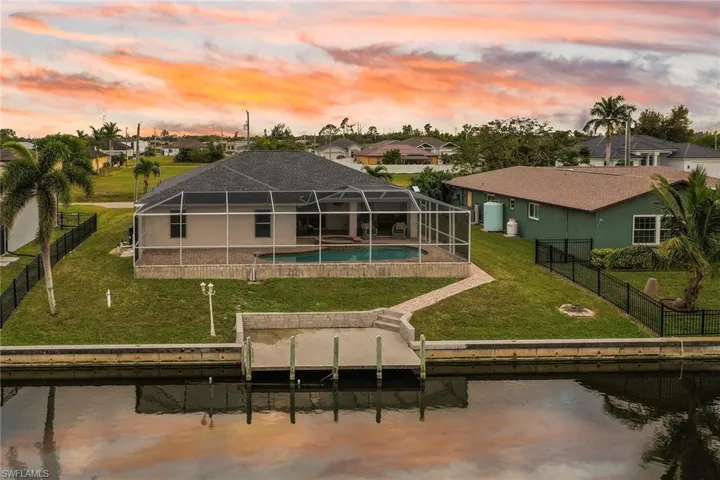 Back house at dusk with glass enclosure, a yard, a fenced in pool, a water view, and a patio