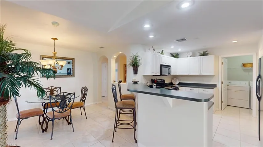 Kitchen with white cabinetry, decorative light fixtures, washer / dryer, a breakfast bar, and black appliances