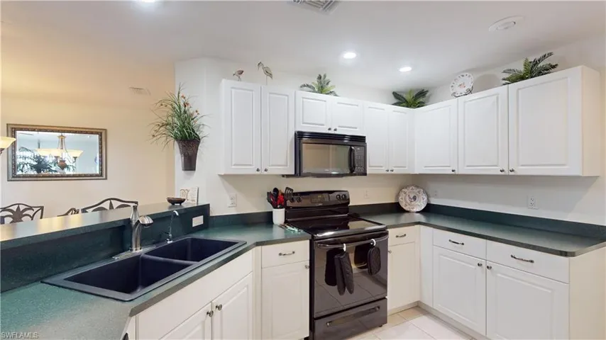 Kitchen featuring white cabinetry, sink, kitchen peninsula, light tile patterned flooring, and black appliances