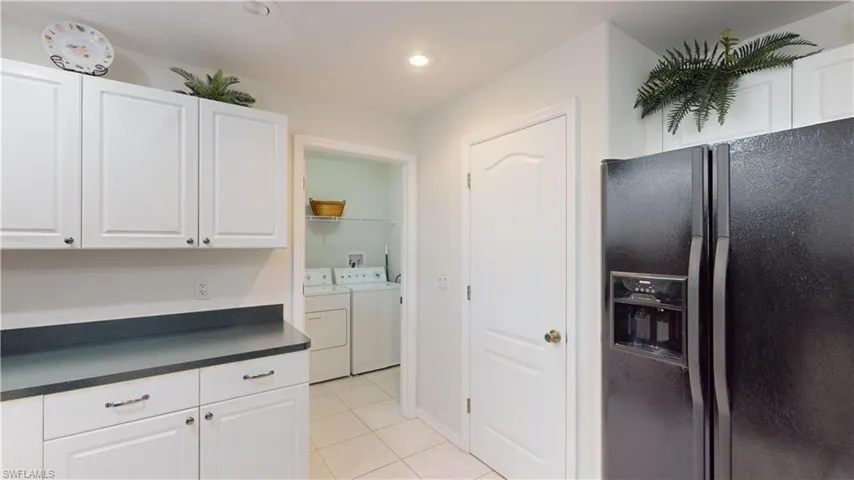 Kitchen with white cabinets, light tile patterned flooring, black fridge, and washing machine and clothes dryer