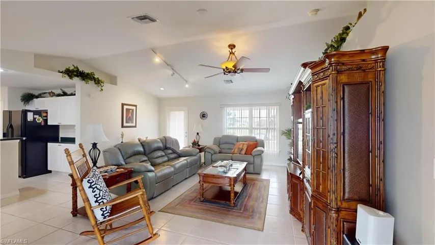 Living room with ceiling fan, light tile patterned flooring, rail lighting, and vaulted ceiling