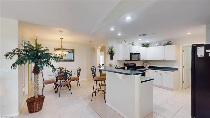 Kitchen with an inviting chandelier, black appliances, white cabinets, light tile patterned floors, and decorative light fixtures