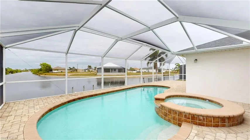 View of swimming pool featuring glass enclosure, an in ground hot tub, a water view, and a patio