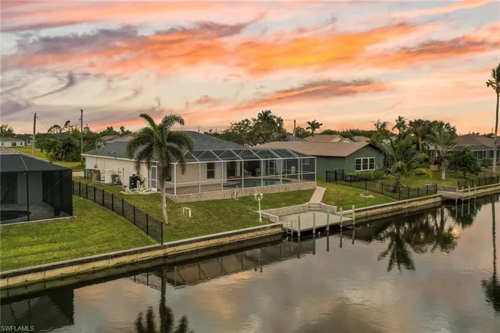 Back house at dusk featuring glass enclosure, a water view, and a yard