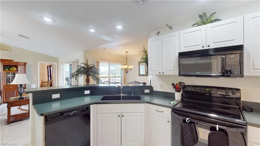 Kitchen featuring kitchen peninsula, sink, black appliances, an inviting chandelier, and white cabinets