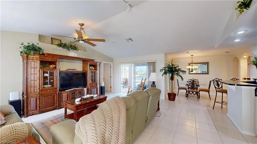 Tiled living room with ceiling fan with notable chandelier and lofted ceiling