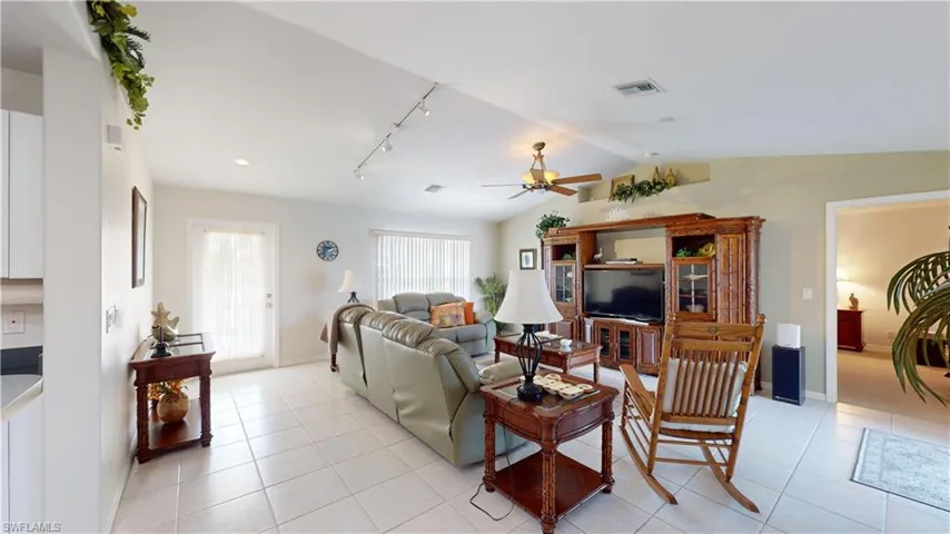 Living room with ceiling fan, light tile patterned floors, track lighting, and vaulted ceiling