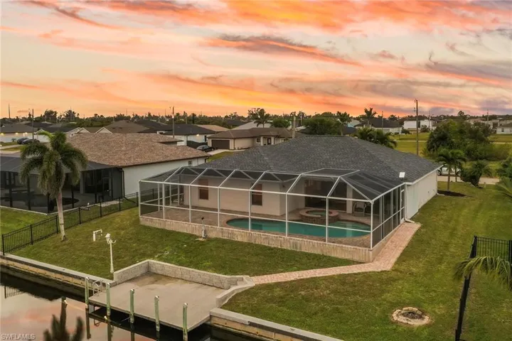 Pool at dusk featuring an in ground hot tub, a lanai, a boat dock, a patio area, and a yard