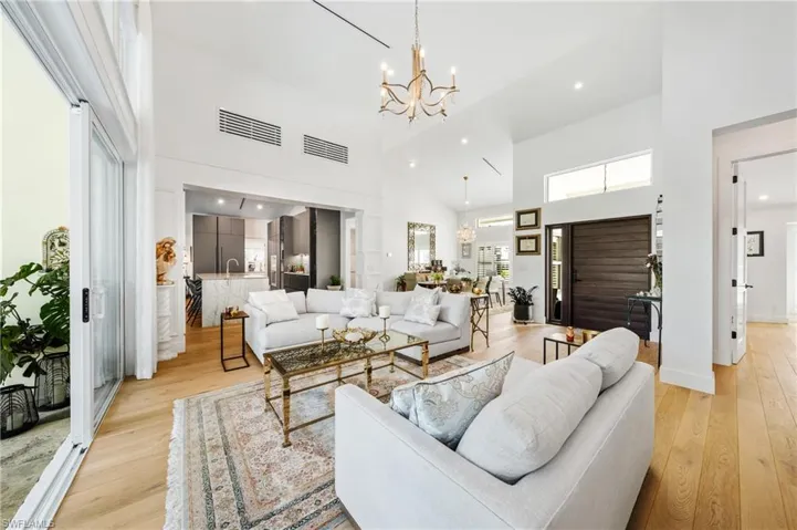 Living room with light wood-type flooring, a notable chandelier, and a towering ceiling