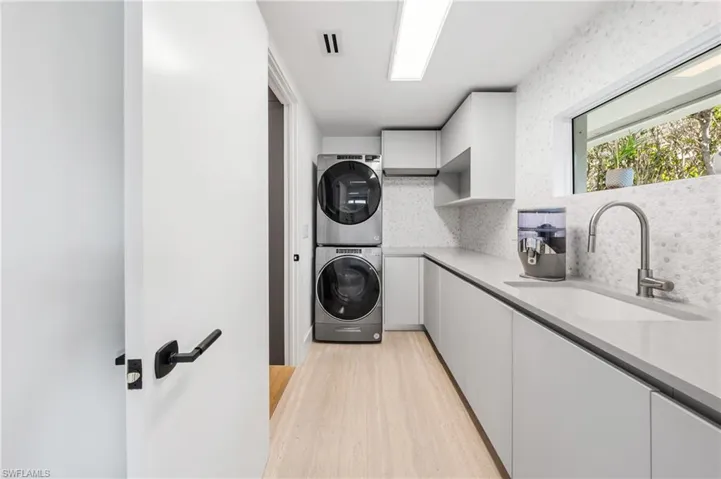 Washroom with sink, stacked washer / drying machine, cabinets, and light hardwood / wood-style floors