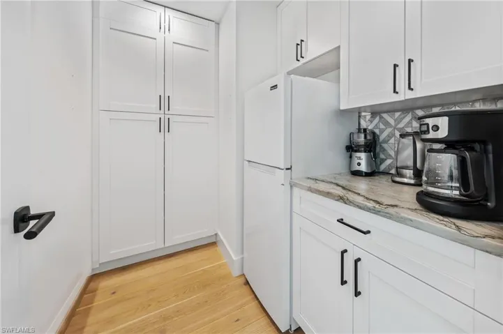 Kitchen featuring white fridge, light hardwood / wood-style flooring, white cabinetry, light stone countertops, and tasteful backsplash