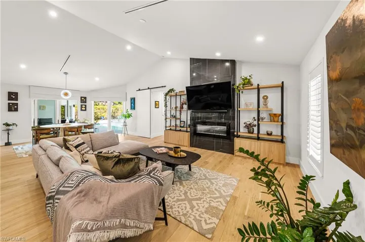 Living room with light wood-type flooring, high vaulted ceiling, a fireplace, and a barn door