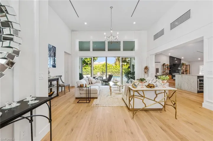 Living room with wine cooler, light wood-type flooring, an inviting chandelier, and a towering ceiling