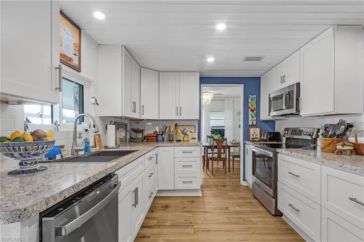 Kitchen featuring white cabinetry, stainless steel appliances, decorative backsplash, light wood-type flooring, and sink