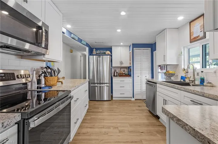 Kitchen with appliances with stainless steel finishes, tasteful backsplash, sink, light hardwood / wood-style floors, and white cabinetry