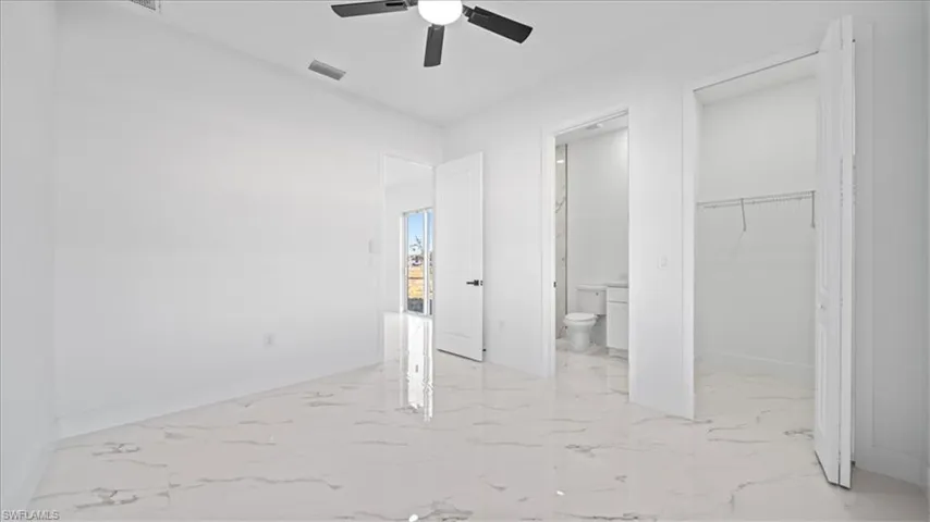 Unfurnished bedroom featuring a walk in closet, light marble finish floors, a ceiling fan, and ensuite bath