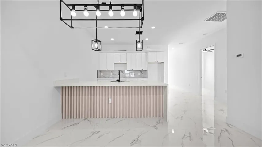 Kitchen with light stone countertops, white cabinets, light marble finish floors, a peninsula, and tasteful backsplash