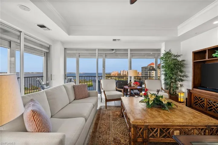 Living room featuring crown molding, freshly painted, beautiful white large tile, tray ceiling and very elegant high-end furniture.