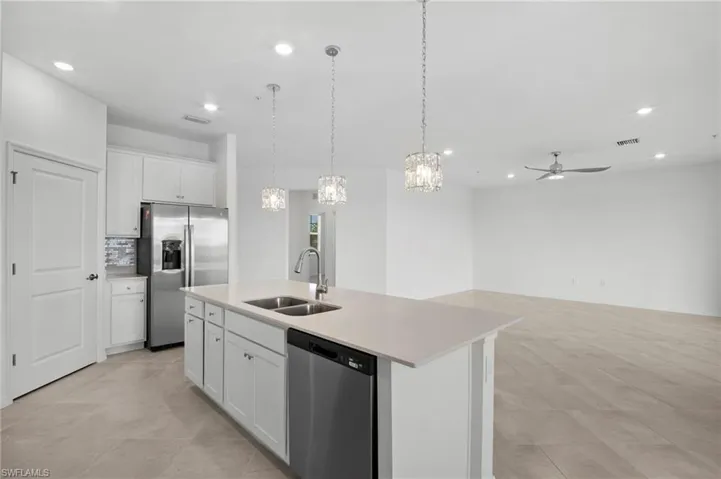 Kitchen featuring white cabinetry, stainless steel appliances, hanging light fixtures, an island with sink, and open floor plan