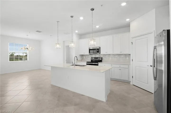 Kitchen with a center island with sink, white cabinets, stainless steel appliances, pendant lighting, and decorative backsplash
