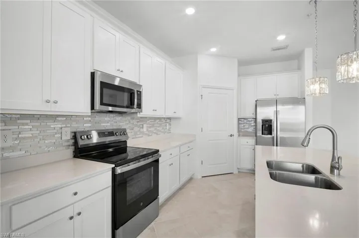 Kitchen with appliances with stainless steel finishes, hanging light fixtures, white cabinetry, decorative backsplash, and light stone countertops