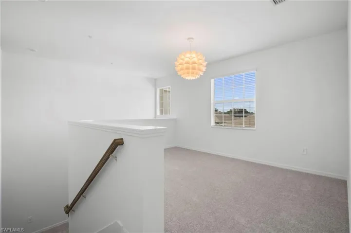 Unfurnished room featuring light colored carpet and a chandelier