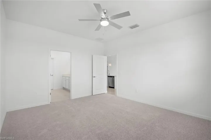 Unfurnished bedroom featuring light carpet, a ceiling fan, and connected bathroom