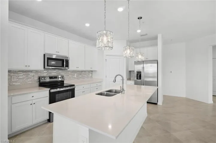 Kitchen with white cabinets, stainless steel appliances, a kitchen island with sink, pendant lighting, and tasteful backsplash