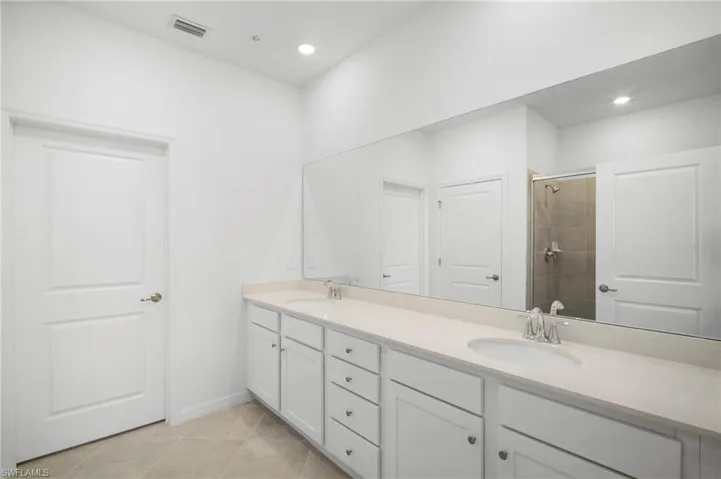 Bathroom featuring double vanity, a shower stall, light tile patterned floors, and recessed lighting