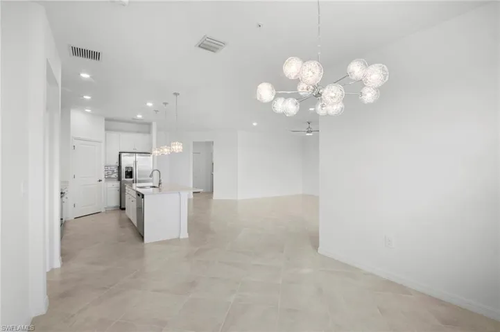 Kitchen with a chandelier, a kitchen island with sink, pendant lighting, white cabinets, and open floor plan
