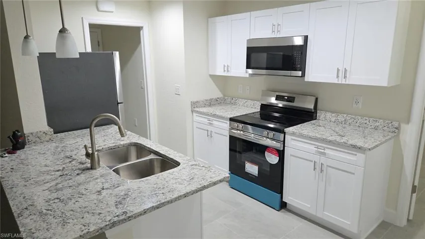 Kitchen featuring stainless steel appliances, pendant lighting, white cabinets, and light stone counters