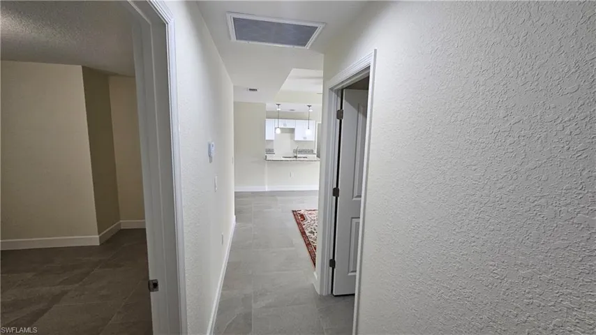 Hallway with a textured wall, tile patterned floors, and baseboards