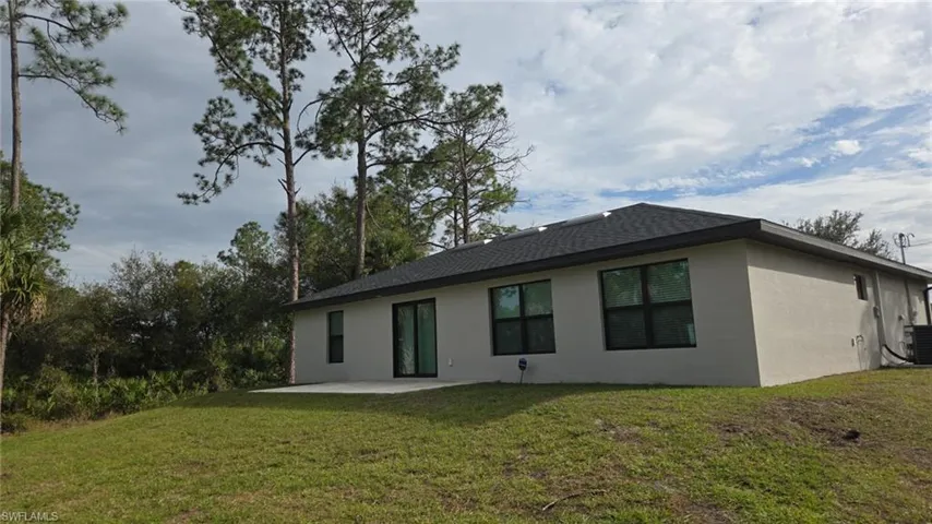 Back of house with stucco siding, a patio, a yard, and a shingled roof