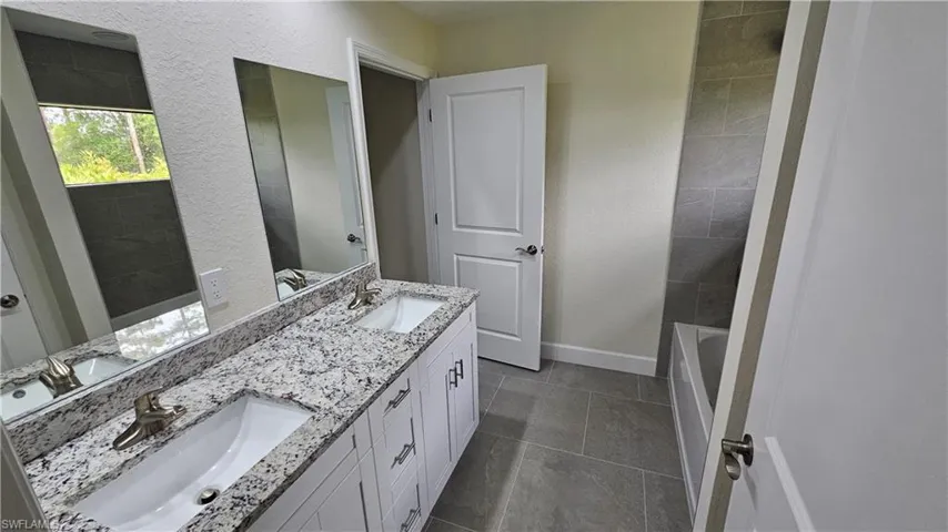 Bathroom with double vanity, baseboards, tile patterned flooring, and a tub