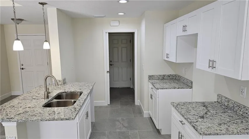 Kitchen with a sink, baseboards, light stone countertops, recessed lighting, and white cabinets