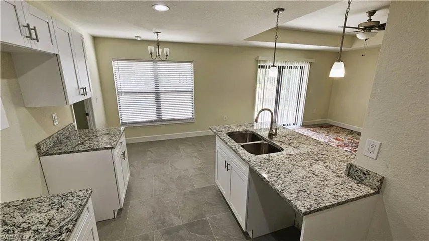 Kitchen with a sink, white cabinetry, light stone counters, decorative light fixtures, and recessed lighting