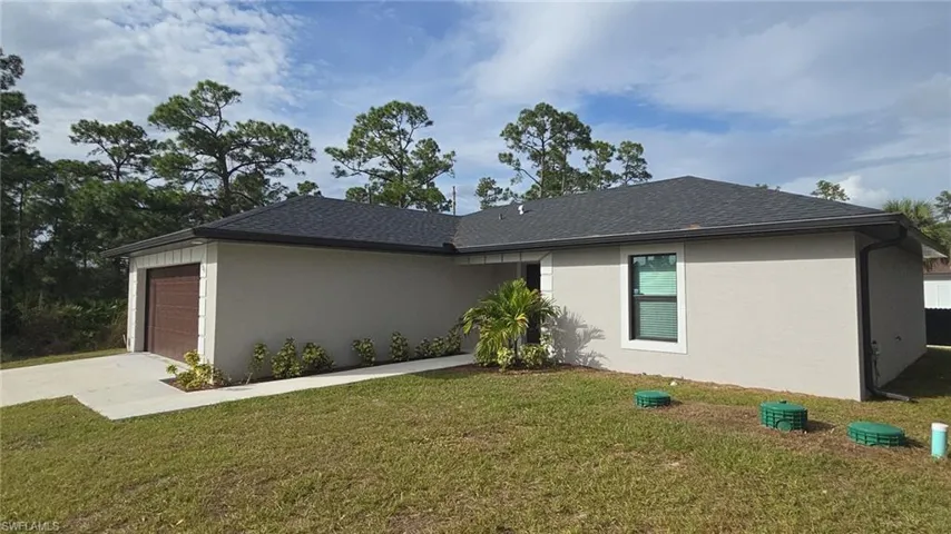 View of side of property featuring a lawn, stucco siding, concrete driveway, and a garage